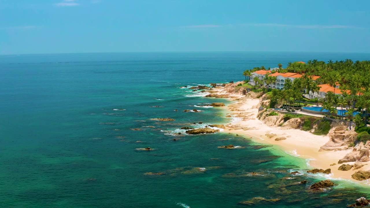 Wide aerial coastline with open turquoise water and a resort beach at upper right.