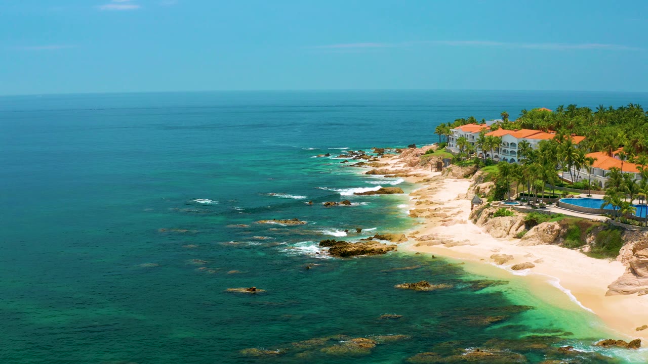 Aerial view of waves breaking around rocks along a sandy Palmilla Beach shoreline.