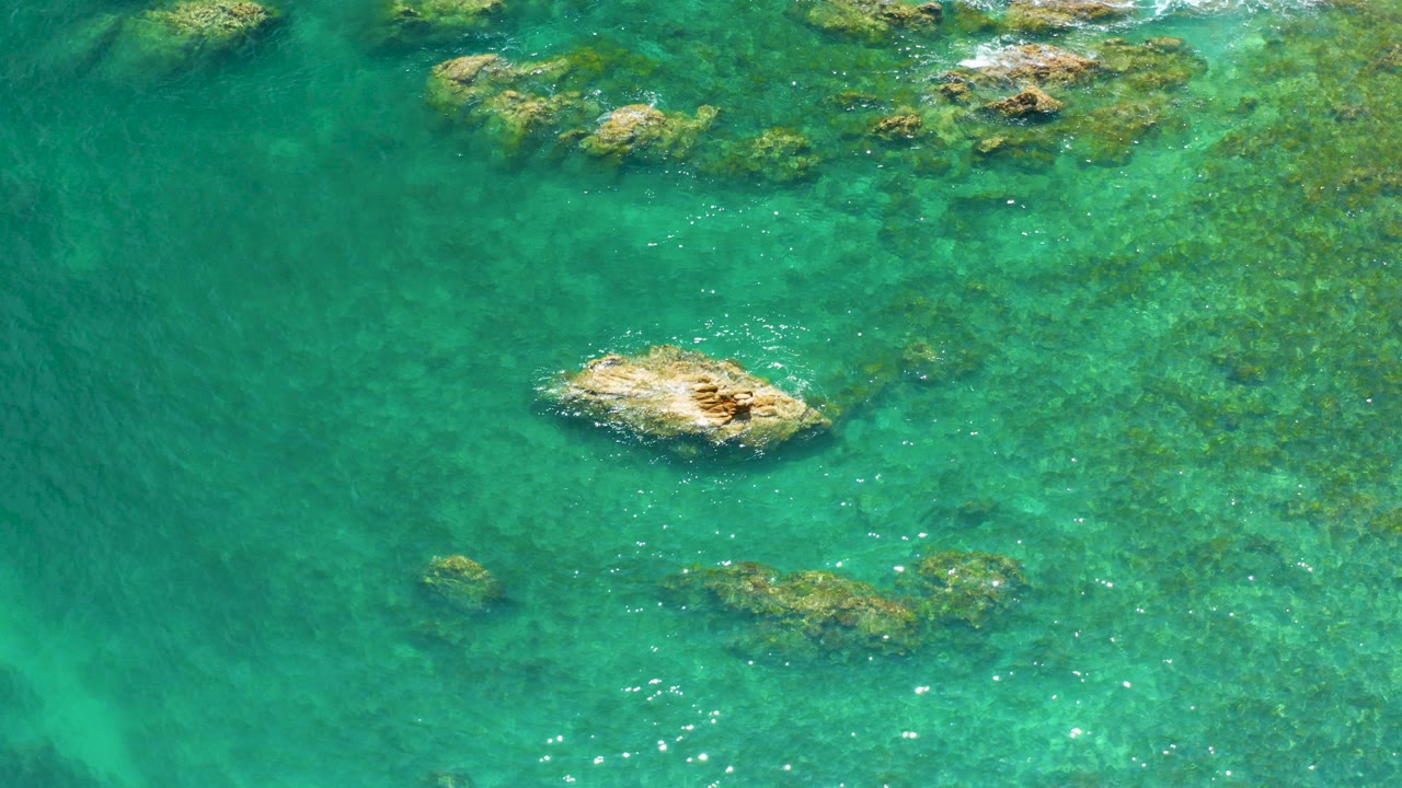 Top-down view of turquoise water and tan coastal rocks.