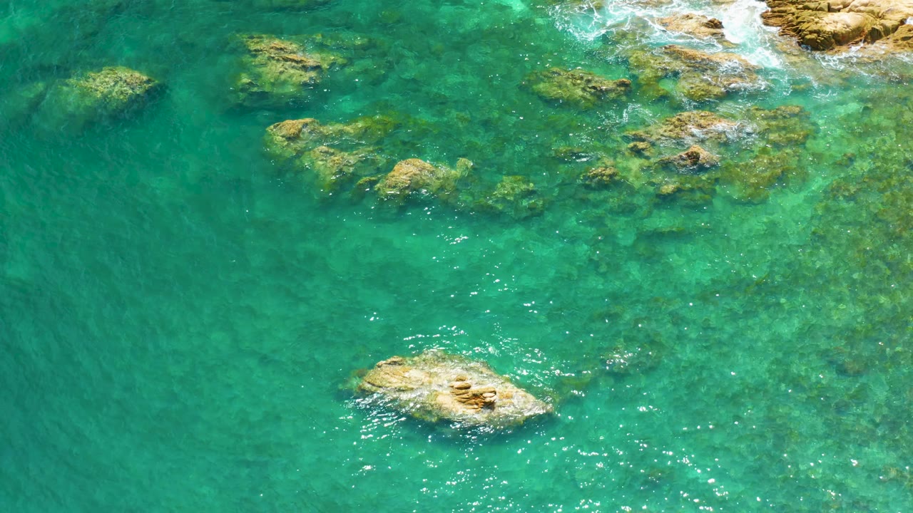 A second overhead frame shows Palmilla Beach water with the larger lower rock slightly farther right, scattered submerged rocks, bright surface glints, and no visible people.