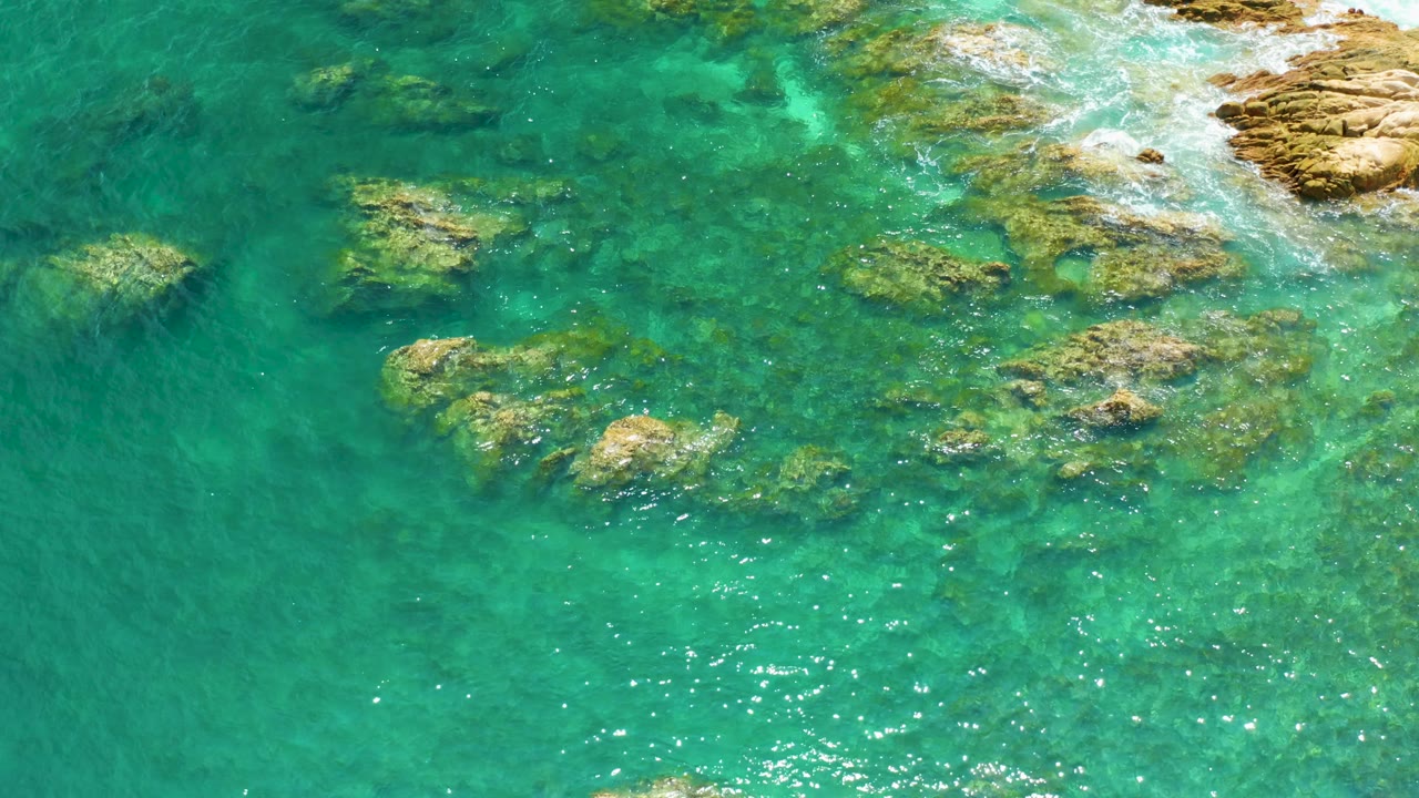 Aerial view of reef shallows at Palmilla Beach, Baja California Sur, with pale foam brushing the rocky edge at the upper right and no visible people.