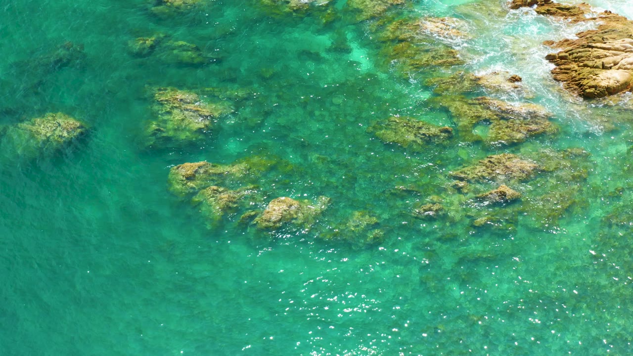 Teal ocean water surrounds reef rocks at Palmilla Beach, with darker open water on the left side and no visible people.