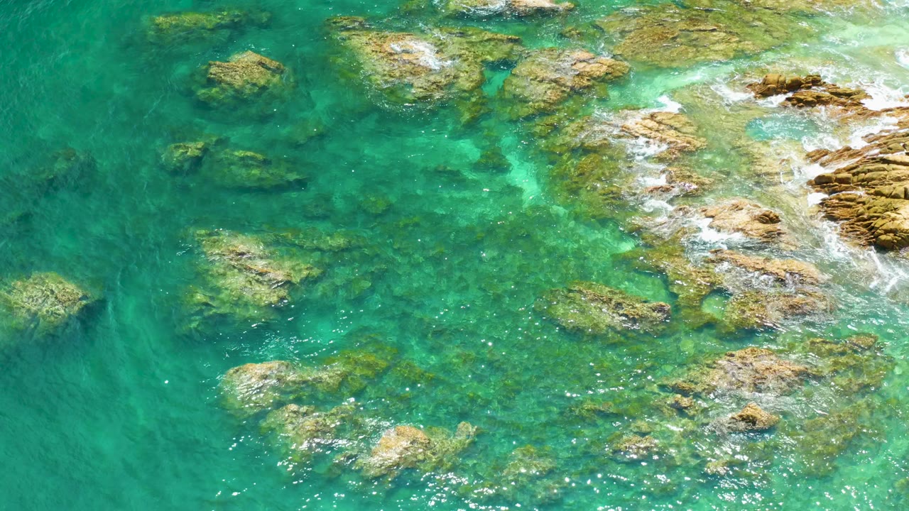 Palmilla Beach water appears bright turquoise around clustered rocks, with white foam breaking along the right side and no visible people.