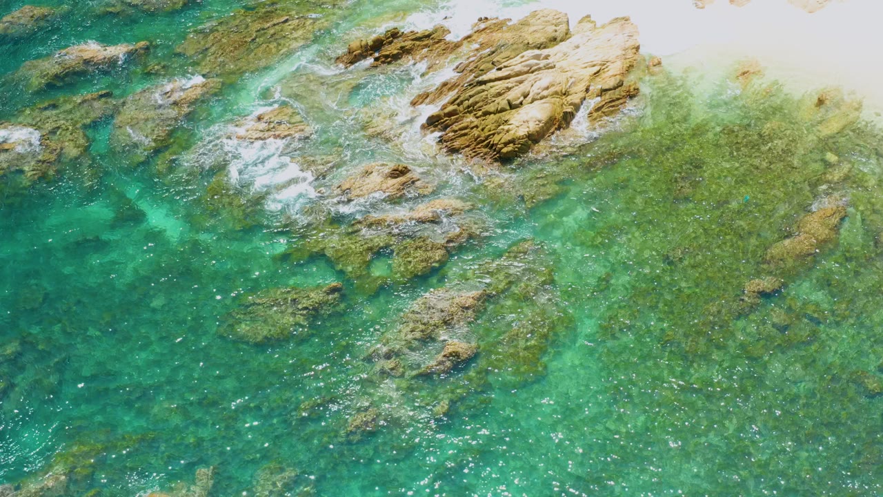 Overhead Palmilla Beach shoreline frame with foamy water wrapping around the upper rock formation, darker turquoise water at left, and no visible people.
