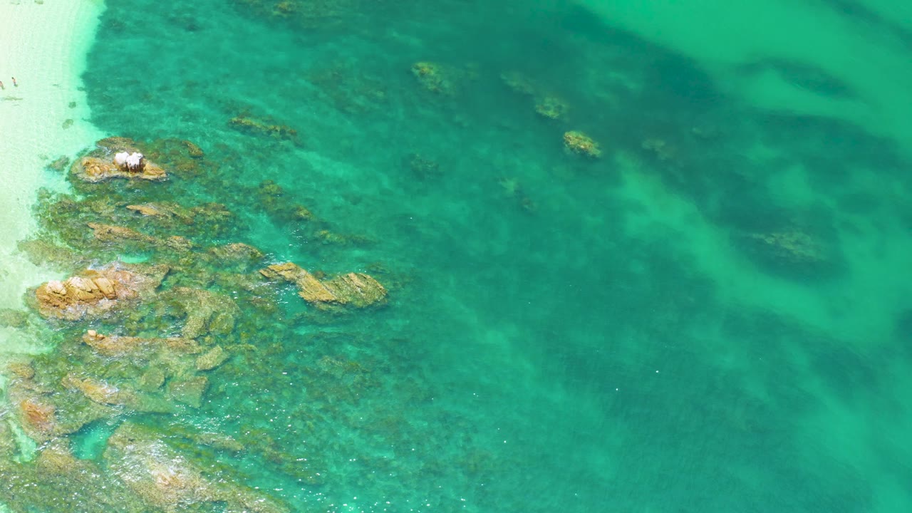Rocky shallows beneath clear green water beside a sand edge.
