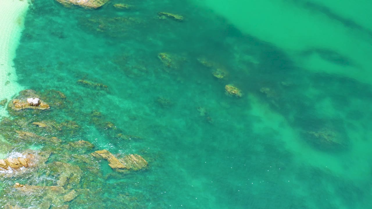 Turquoise shallows with rocky formations near the left edge and open water to the right.