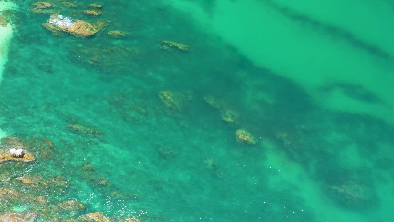 Aqua water at Palmilla Beach fills the frame with darker underwater bands, small rock patches near the upper left, and no visible people.