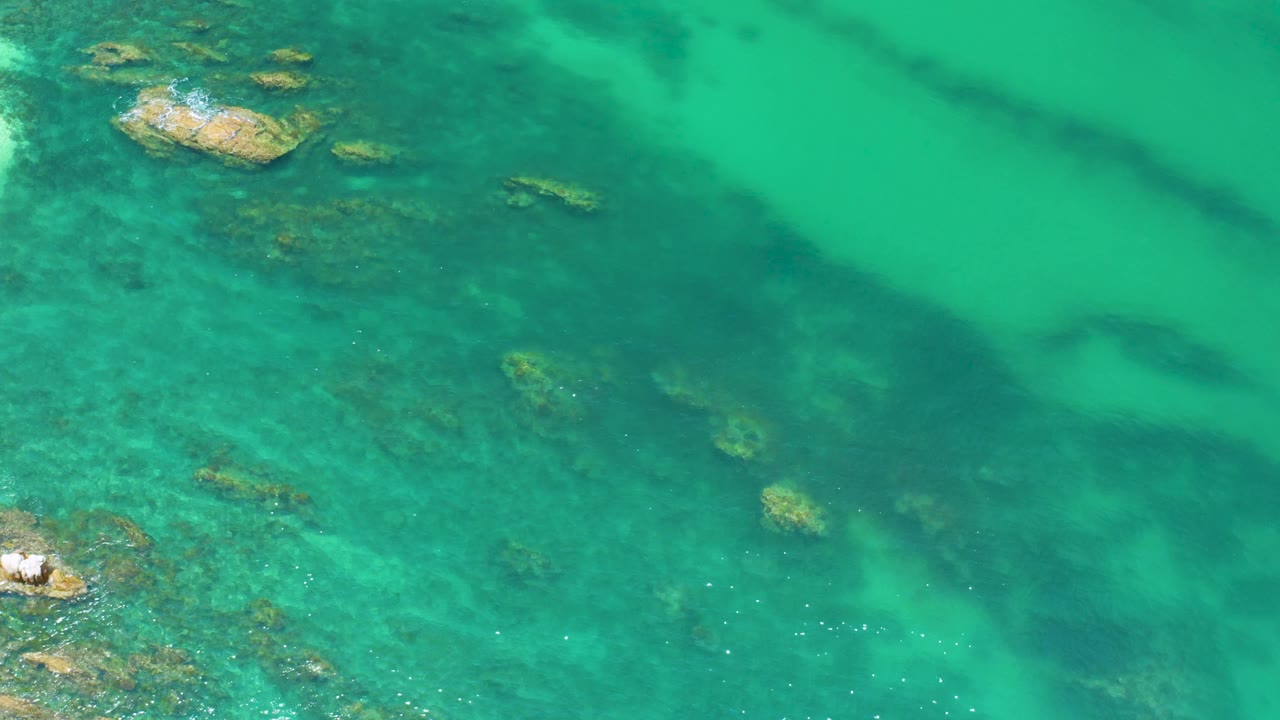 Rocky shallows under turquoise water with white wash on small outcrops.
