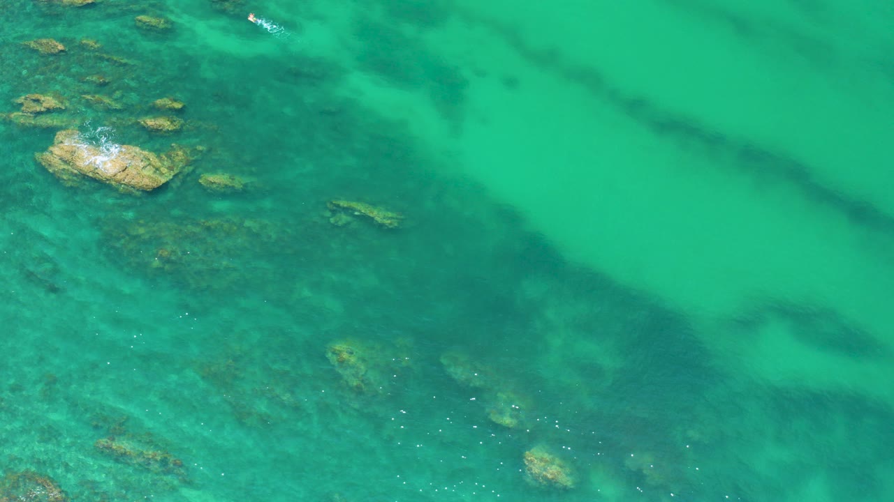 Overhead view of turquoise water at Palmilla Beach, Baja California Sur, with scattered shallow rocks near the upper left and no visible people.