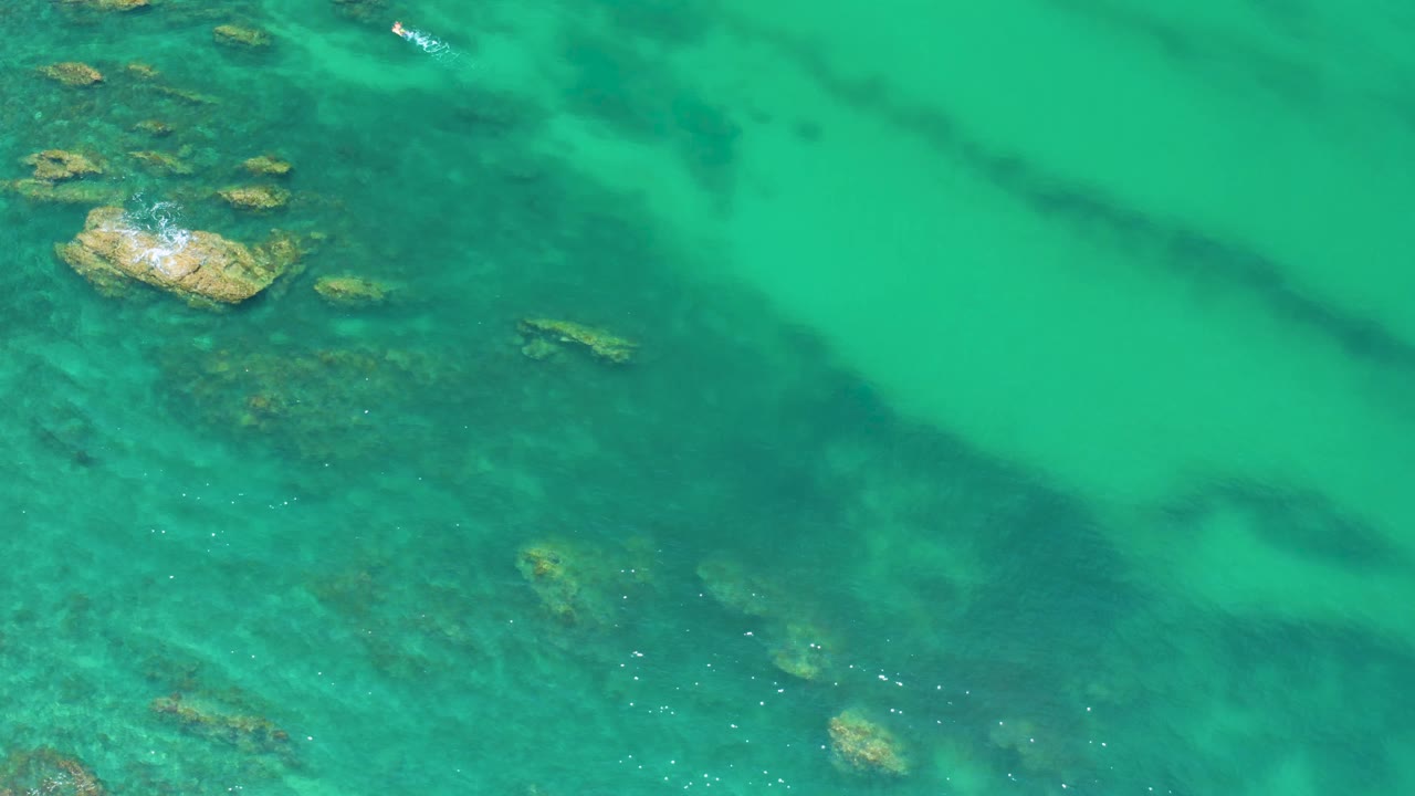 Clear green-blue water with a larger rock near the upper left.