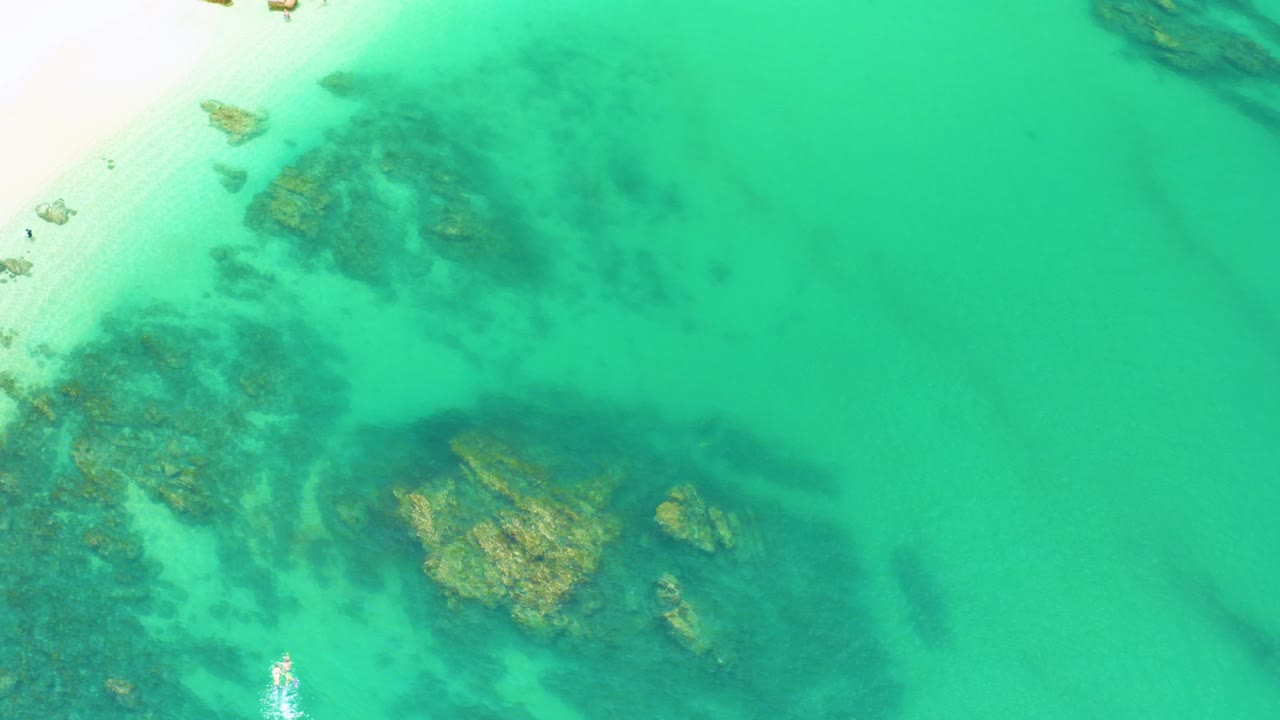 Overhead view at Palmilla Beach, Baja California Sur, showing turquoise water over submerged rocks with a bright sand edge at upper left and no visible people.