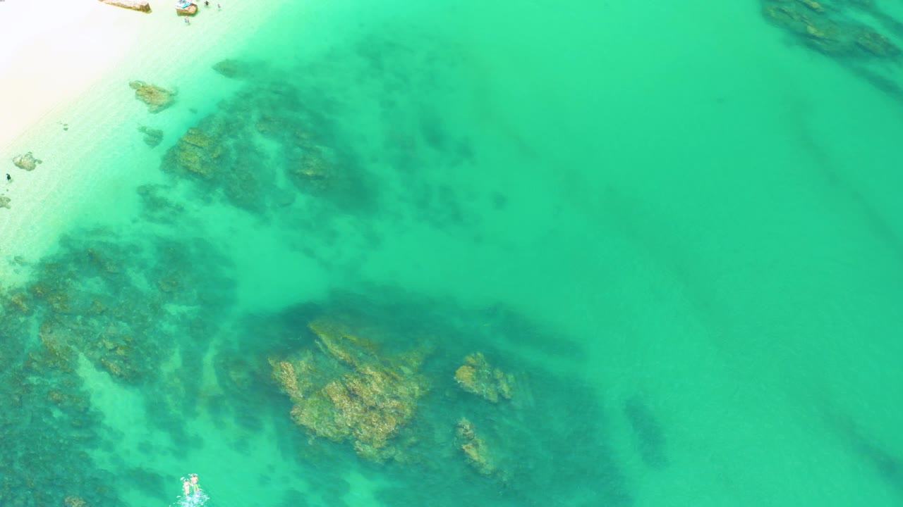 At 0:02, submerged rock clusters sit left of center under bright turquoise water at Palmilla Beach, with more open water filling the right side and no visible people.