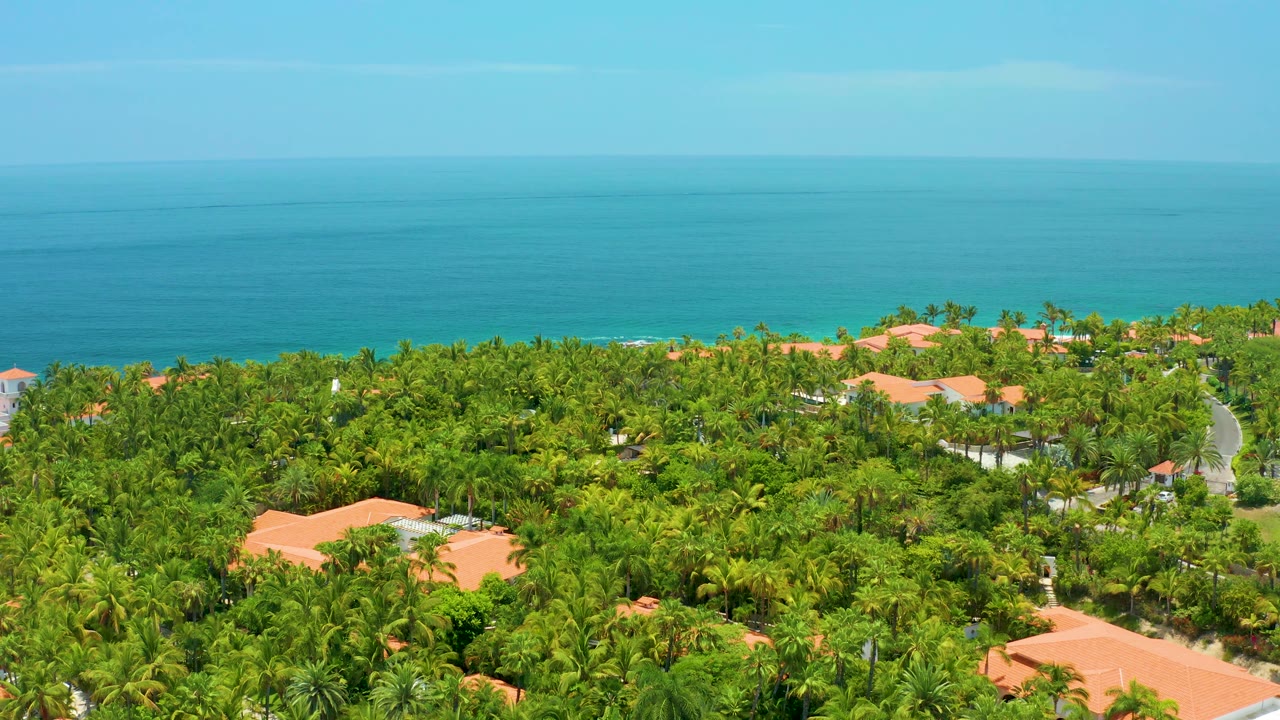 Elevated coastal view with palms, red tile rooftops, and calm sea.