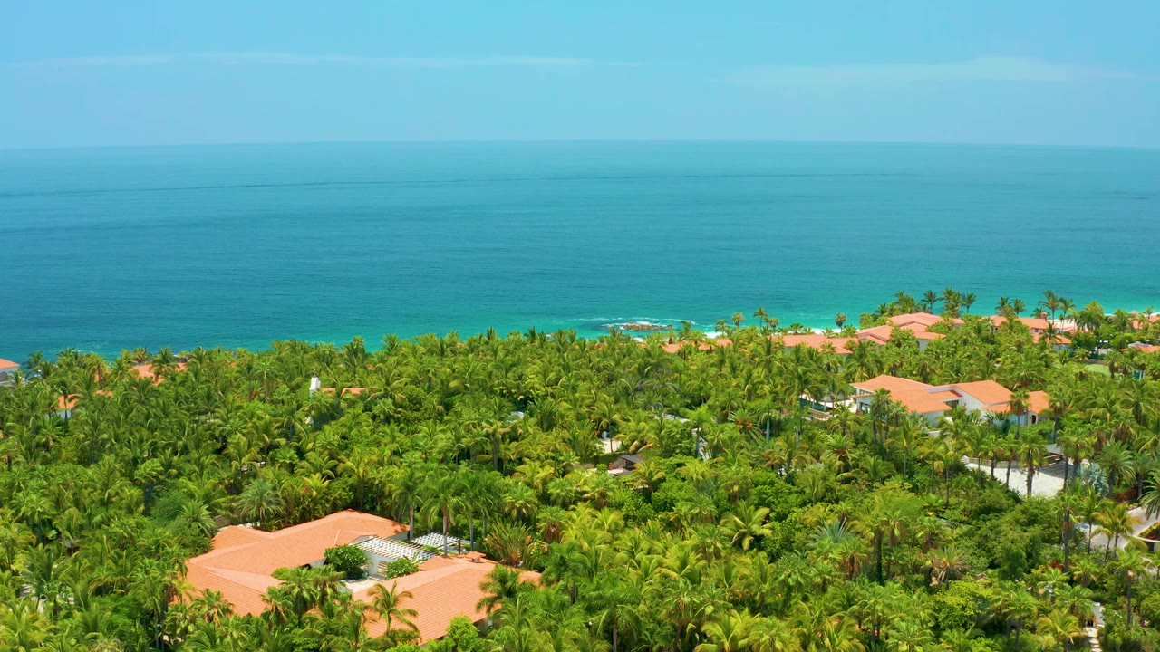 Wide aerial view of tropical homes with ocean behind them.