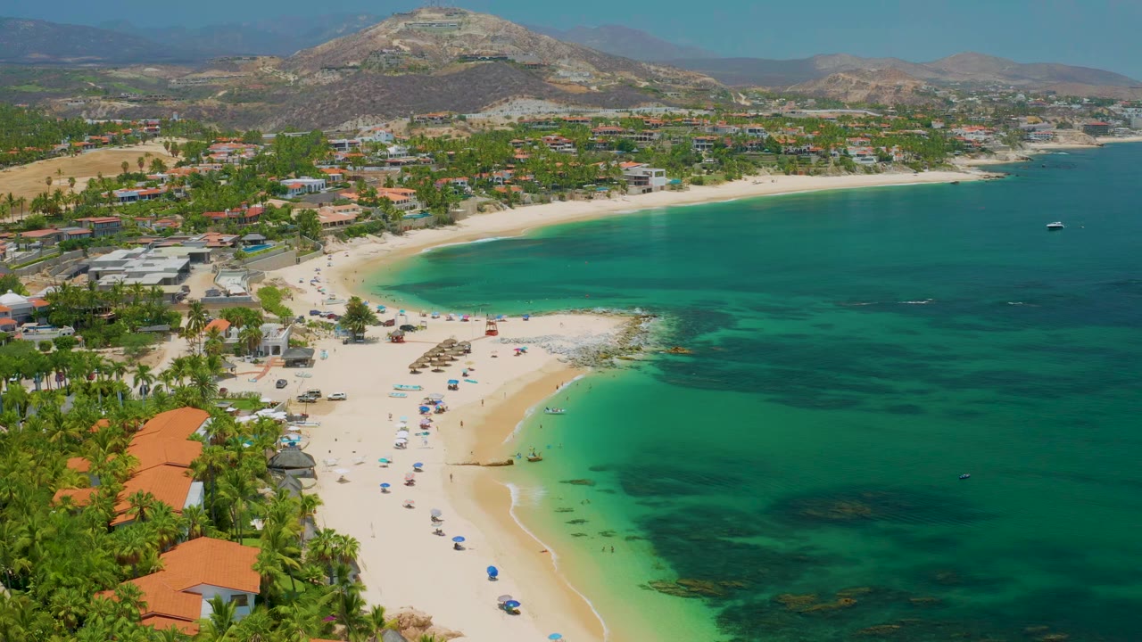 High coastal view of umbrellas on sand beside green-blue water and resort buildings.