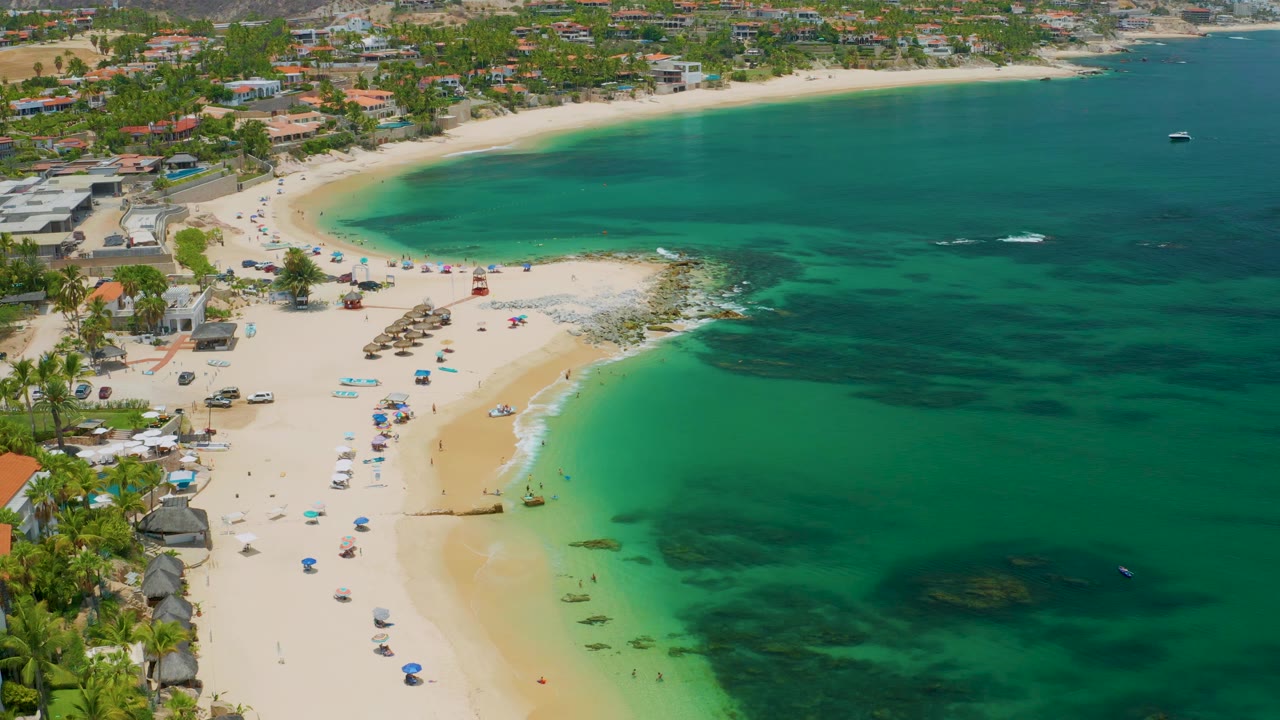 Drone view of beach umbrellas beside clear green-blue water.