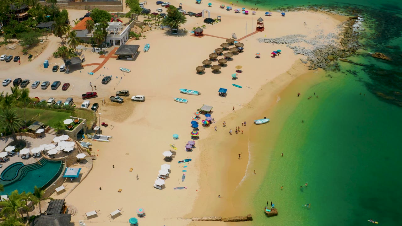Overhead beach scene with swimmers in shallow water and umbrellas on the sand.