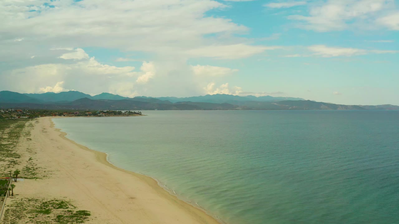 At 0:01, the La Ribera shoreline fills the left side while broad blue-green water extends to the right beneath layered white clouds, with no visible people.