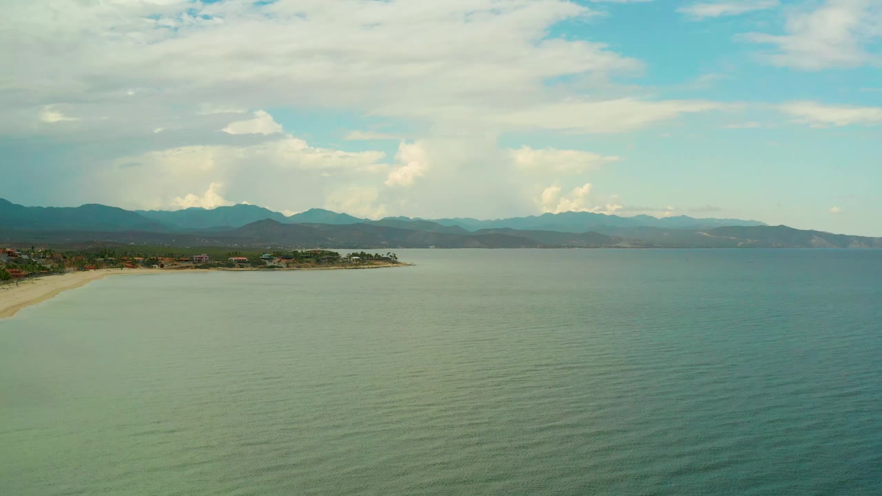 Calm sea beside a sandy shoreline with mountains in the distance.