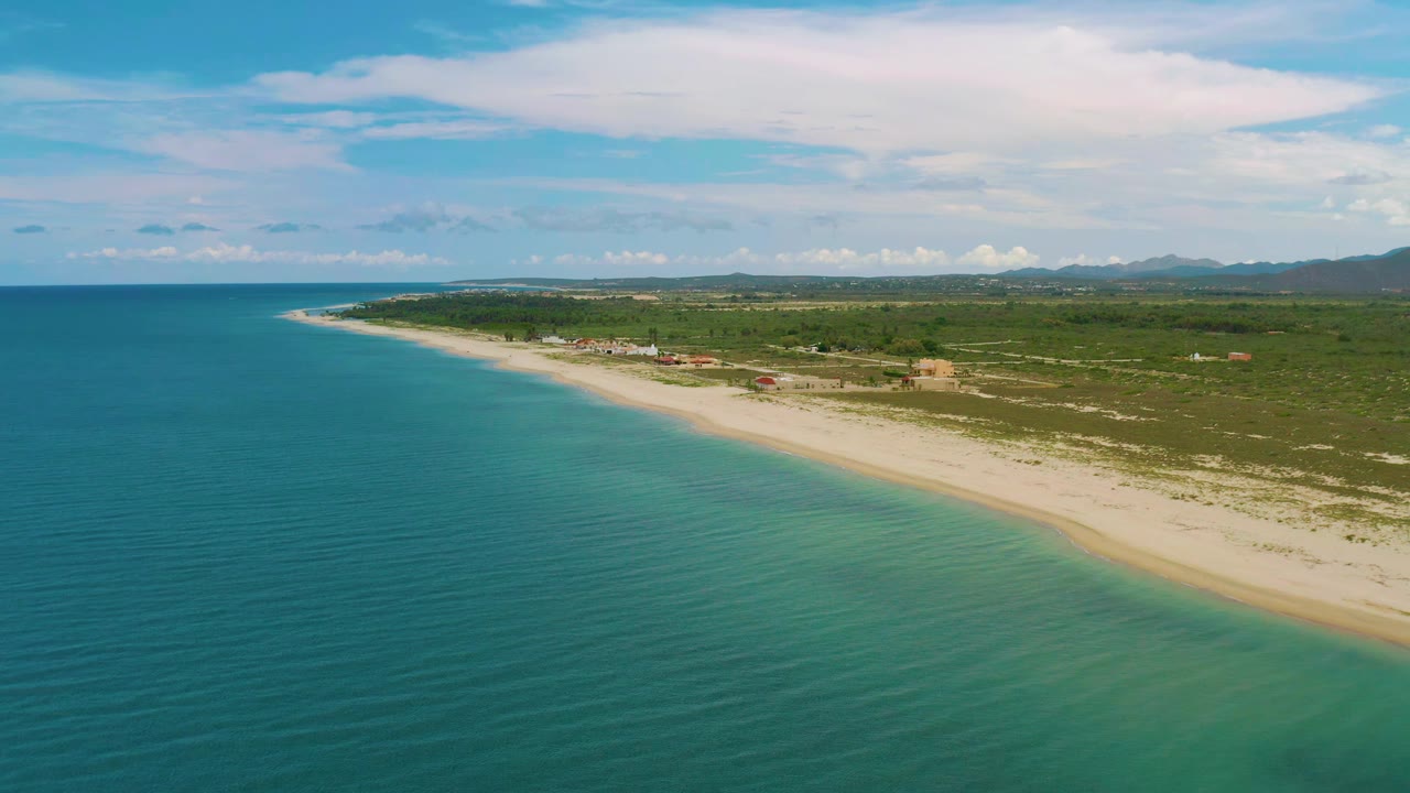 Drone view of turquoise water and a pale beach backed by scrubland.