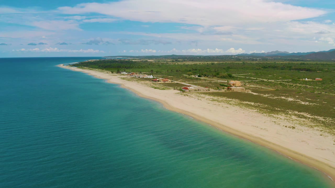 Elevated coastal view with blue-green water, beach, scrubland, and distant hills.