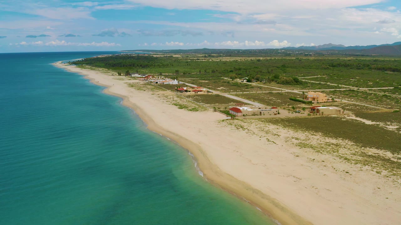 Aerial coastline frame with calm sea, curved beach, and beachside buildings