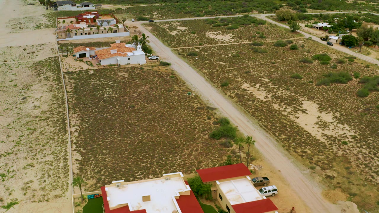 High drone view of a dirt road cutting between scrubland and houses.