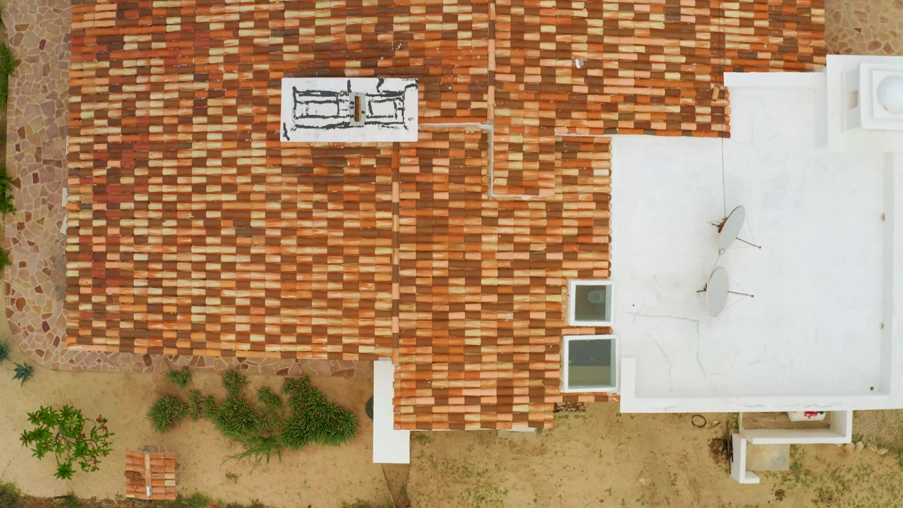 Aerial overhead view in La Ribera, Baja California Sur with the roofline centered, white flat roof to the right, shrubs below the house, and no visible people.