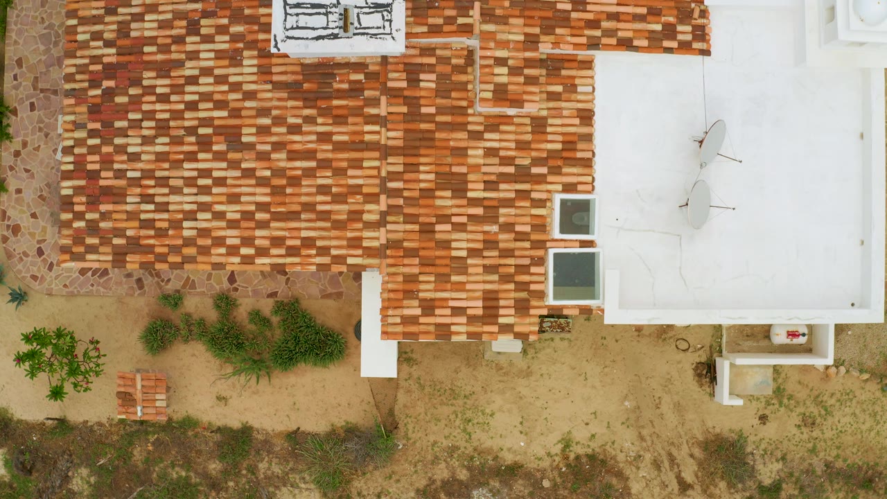 Close overhead view of roof tiles, white roof, shrubs, and outdoor chairs.