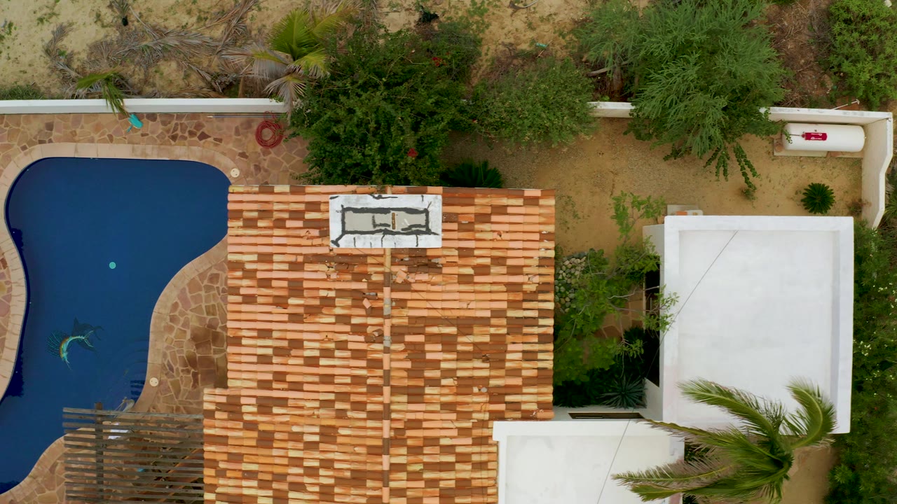 Overhead poolside scene with the blue pool at left and a large roof at center.