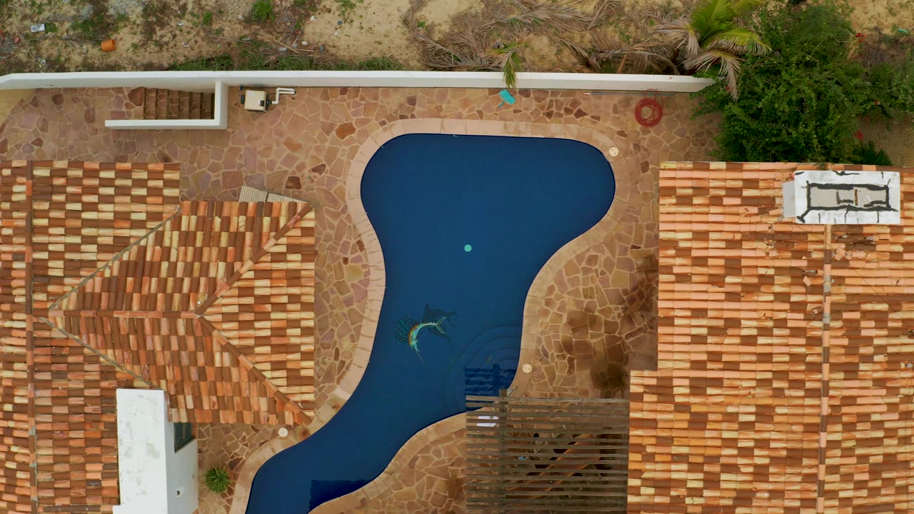 Overhead residential pool framed by roofs, patio stone, and desert ground.