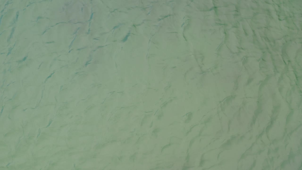 Opaque grey green water fills the first frame in La Ribera, Baja California Sur, with faint diagonal ripple marks and no visible people.