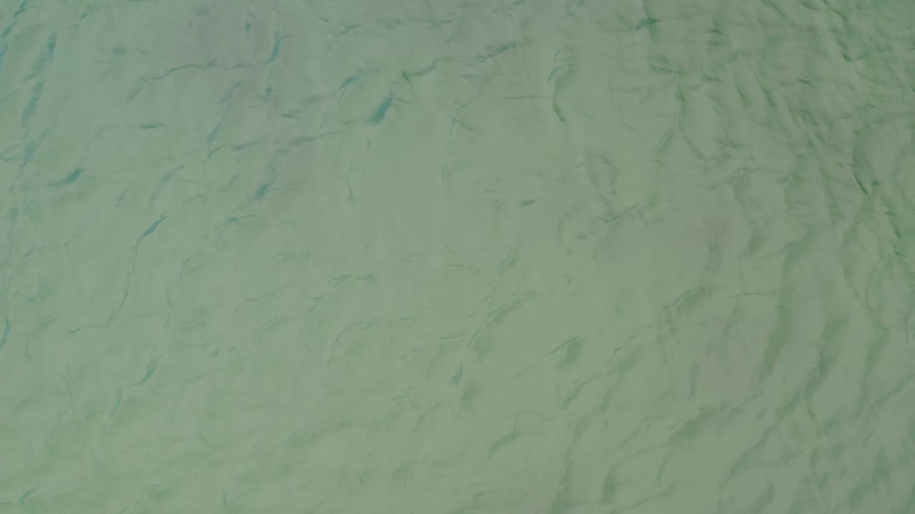 Muted green water fills the frame in La Ribera, Baja California Sur, with thin sinusoidal ripple streaks spread across the surface and no visible people.