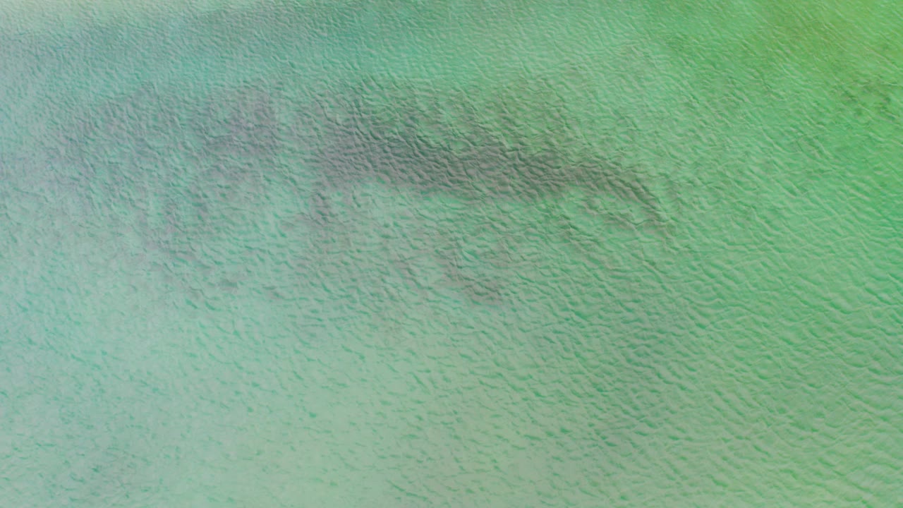 Top-down view of turquoise-green water in La Ribera, Baja California Sur, with fine ripples and no visible people.