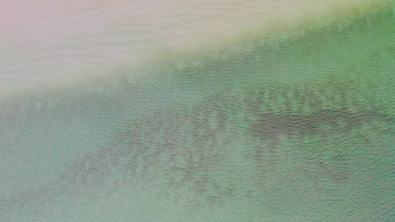 La Ribera coastal water appears as a muted green and turquoise field with pale sand along the upper edge, darker underwater marks through the middle, and no visible people.