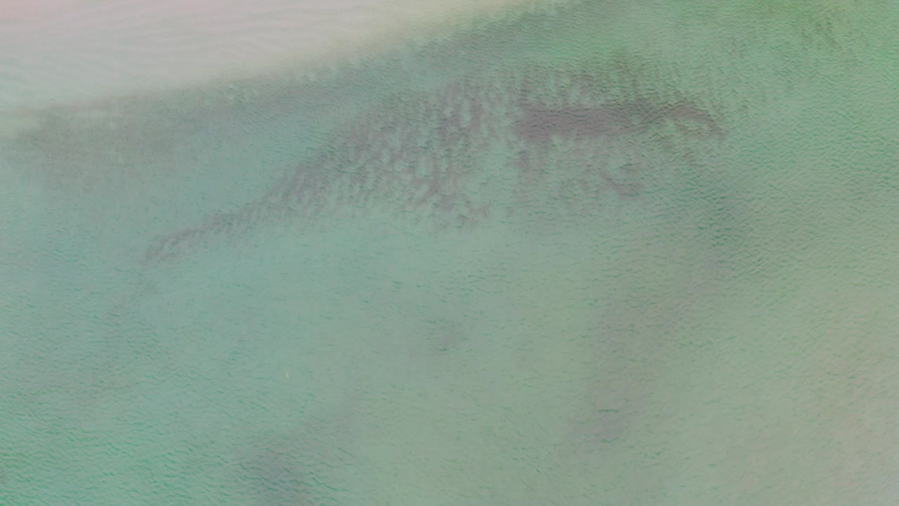 Overhead turquoise sea water with dark submerged patches near a pale sandy edge.