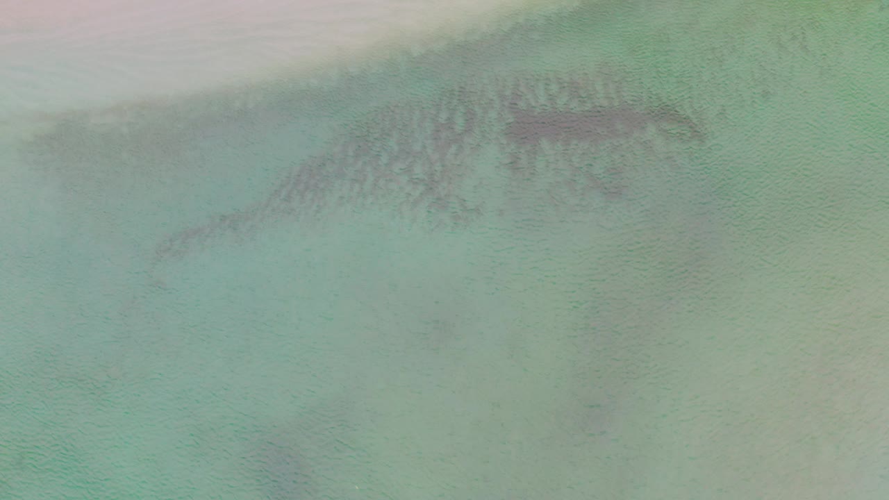 Top-down view of La Ribera sea water with muted turquoise color, darker submerged patches near the upper center, and no visible people.