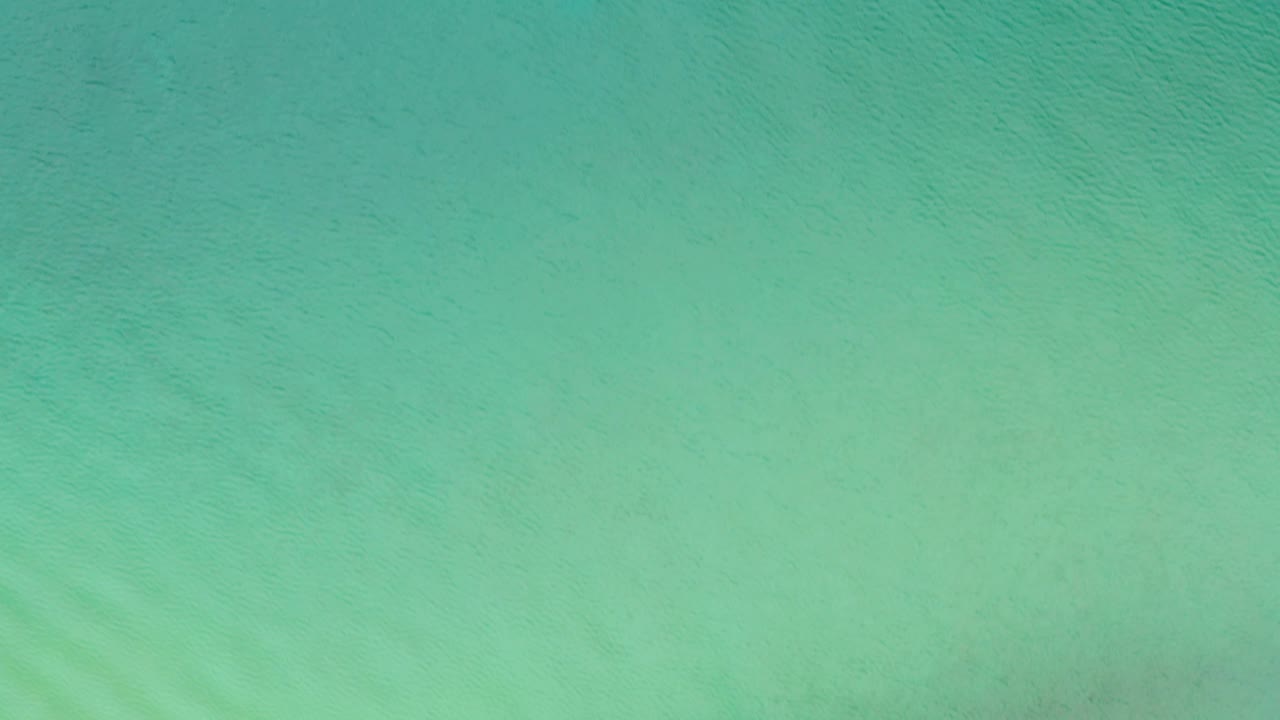 Turquoise sea surface over La Ribera, Baja California Sur, Mexico, with faint darker patches beneath the water and no visible people.