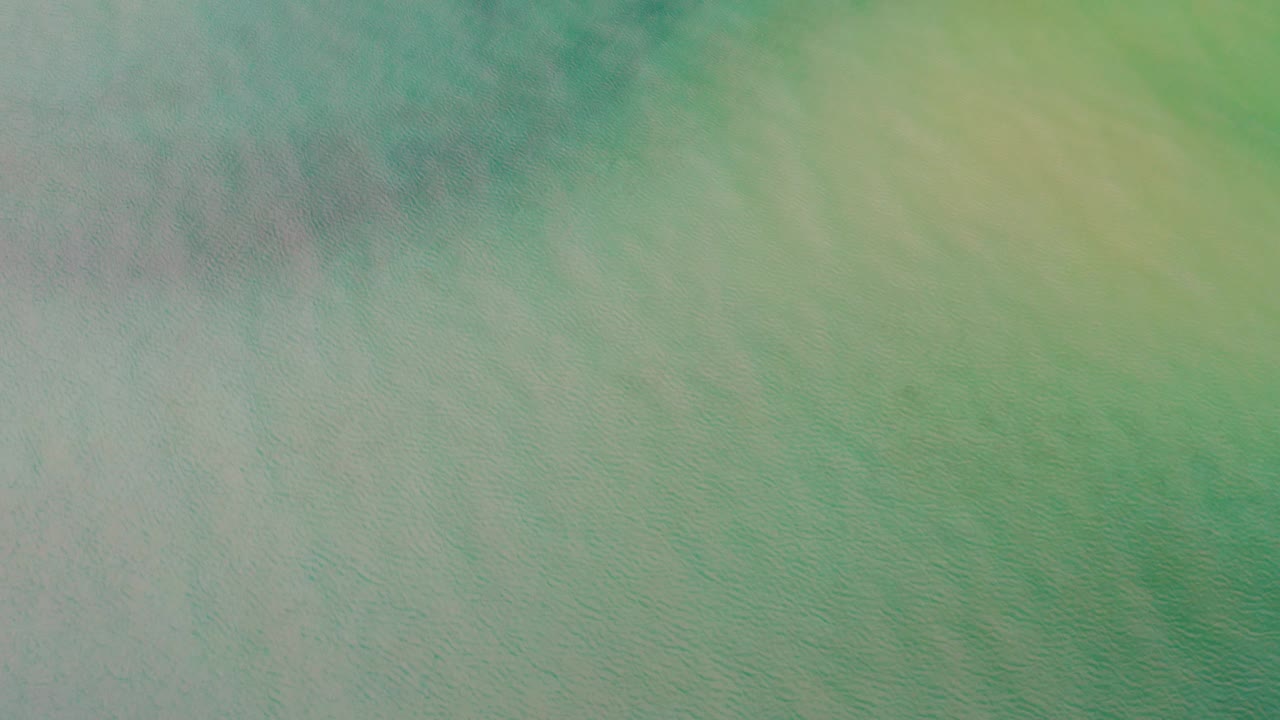 Overhead ocean frame from La Ribera, Baja California Sur, showing soft green water mixed with blue-gray patches and no visible people.