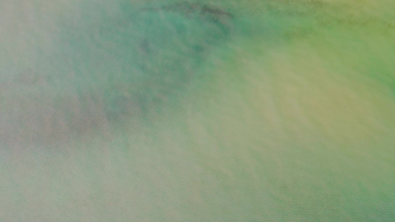 Aerial view in La Ribera, Baja California Sur with turquoise-green water filling the frame and a muted sandy shoreline just visible along the top, with no visible people.