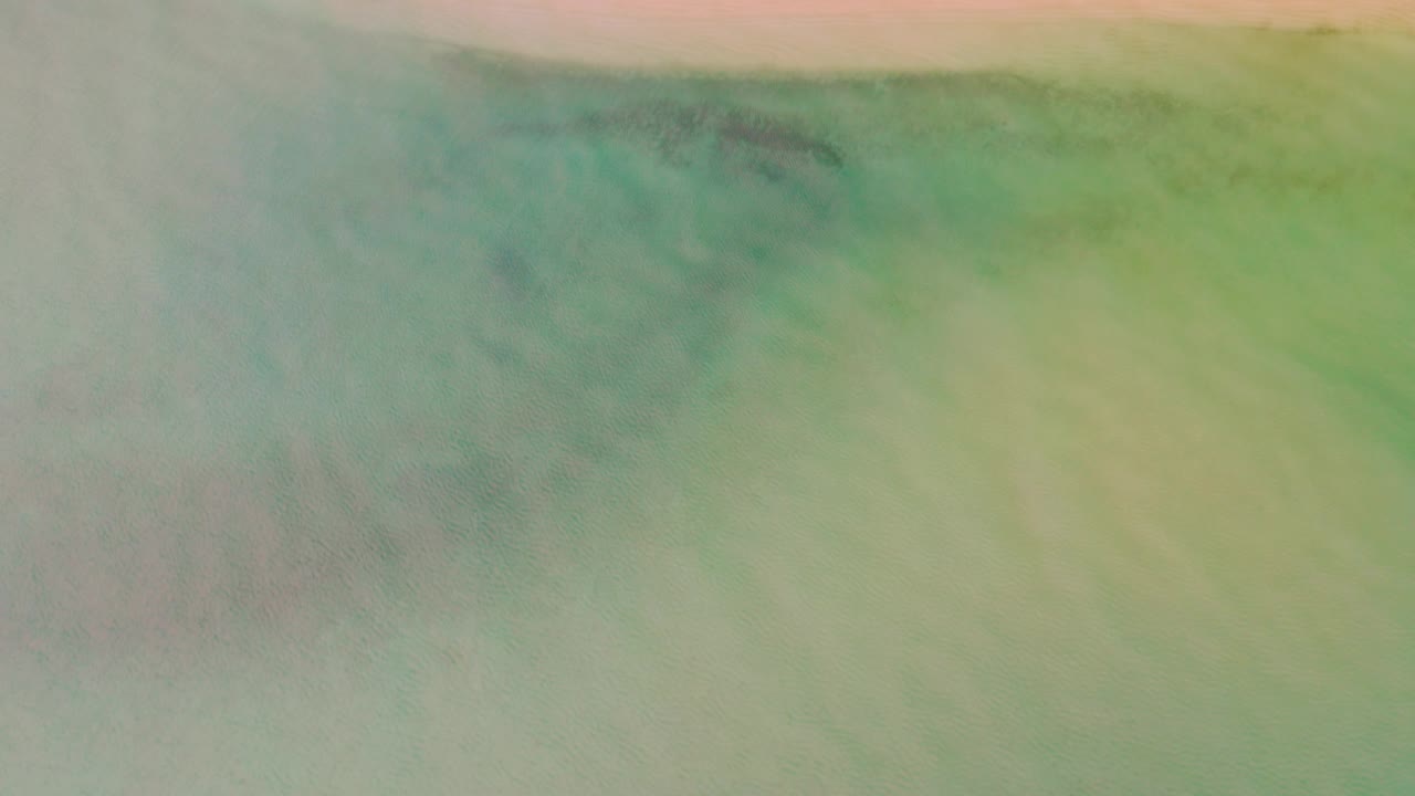 Overhead La Ribera beach frame with green water below, a thin pink beach line across the upper edge, and no visible people or structures.