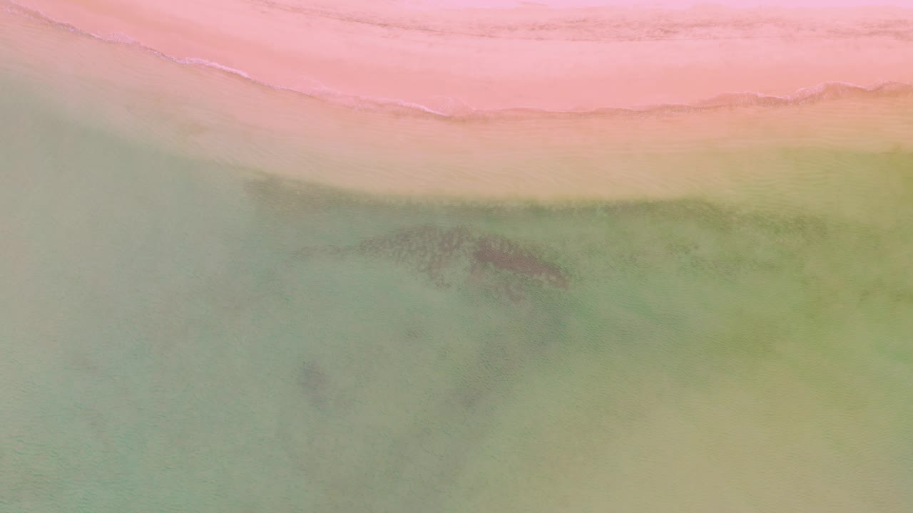 Soft surf line along pink sand and green water