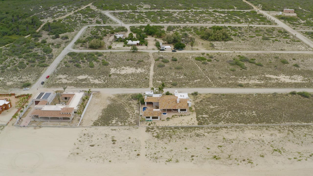 Drone view over beachside houses, scrub lots, and intersecting roads.