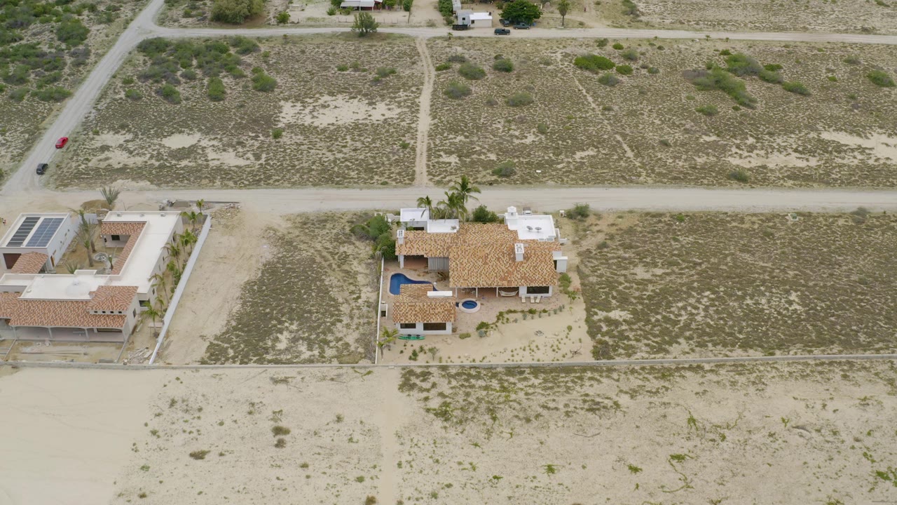 Two houses seen from above beside open sandy land.