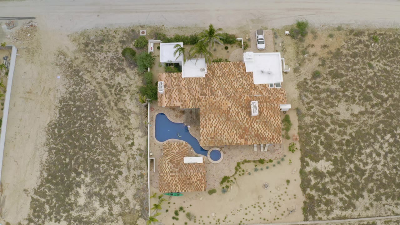 Overhead residential property with pool, tile roof, and sparse landscaping.