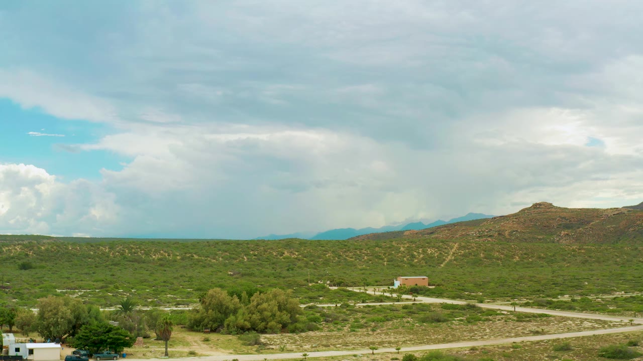 Green open land under a clouded sky with dirt tracks and small rural structures.
