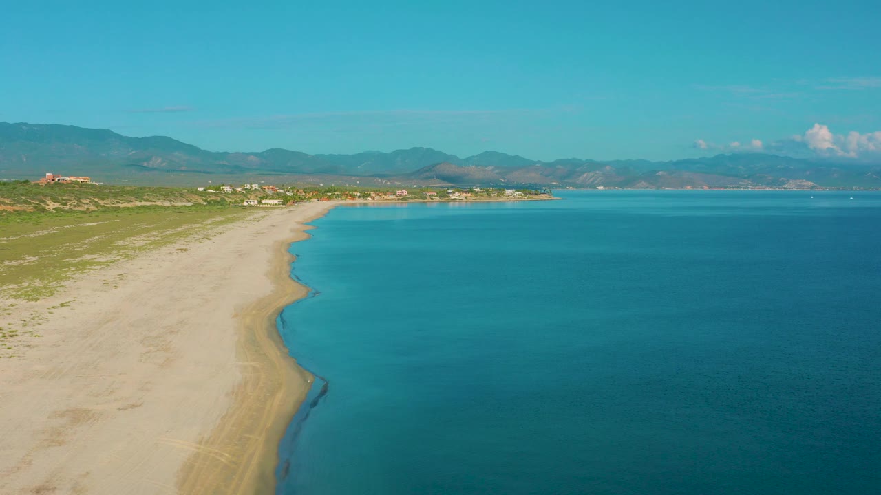 Aerial beach view with shallow water near shore and mountains beyond.