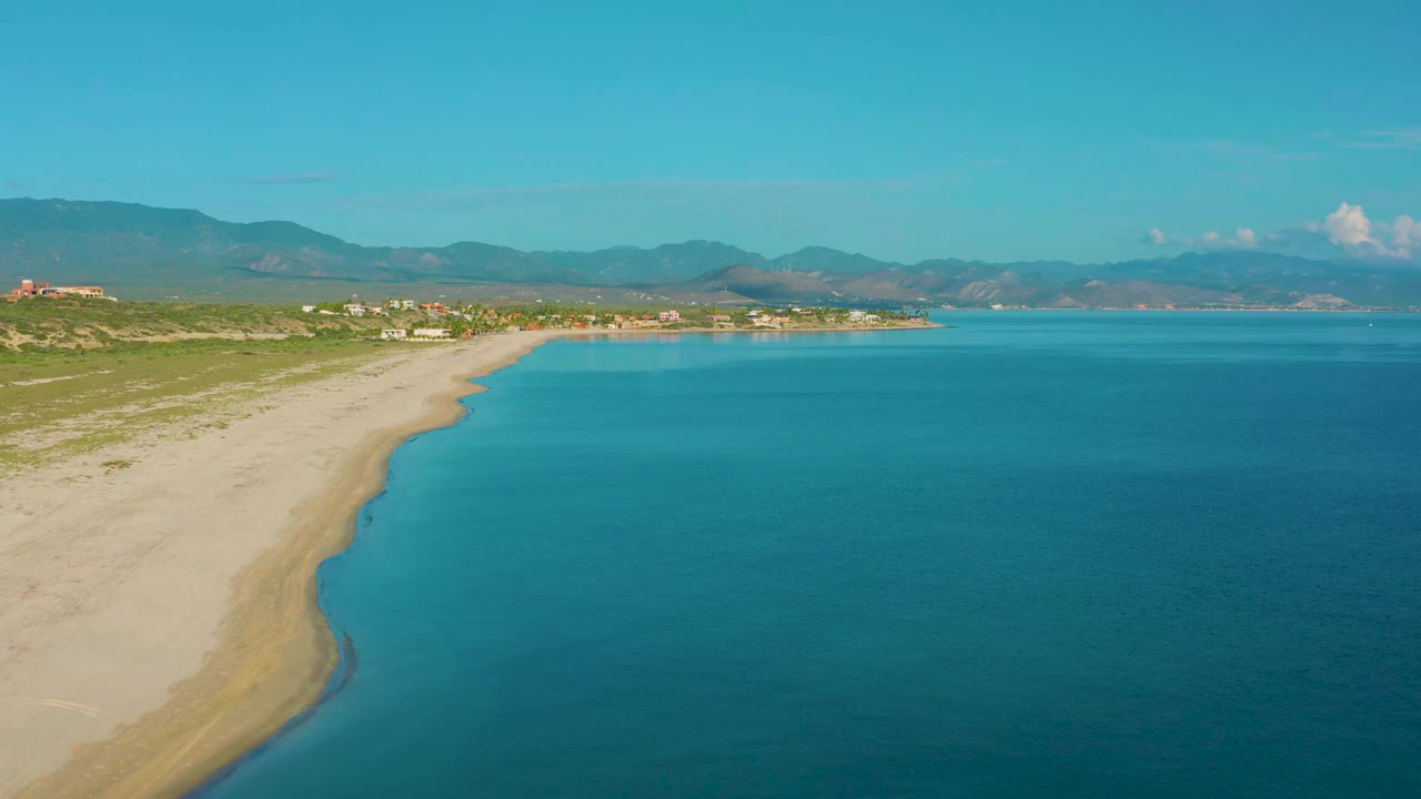 Curving sandbar beach with blue sea and mountain range in the distance