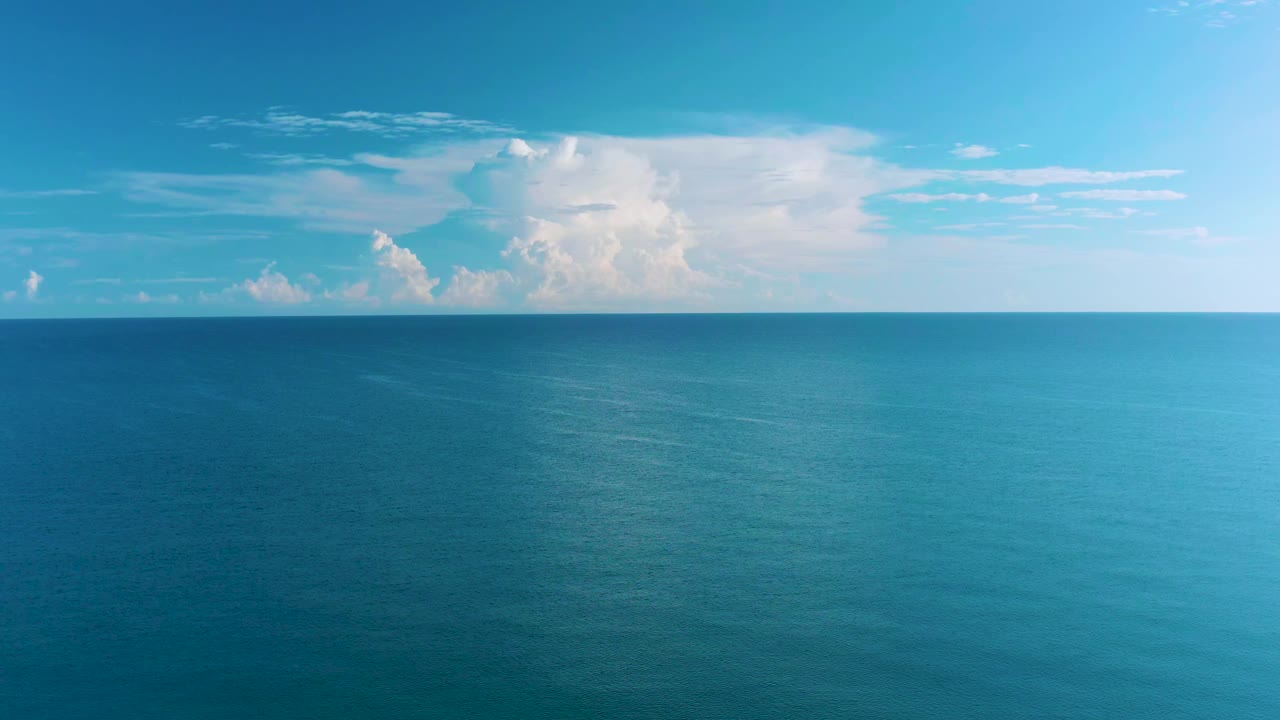 La Ribera ocean view one second in, showing a level horizon, textured blue water, and a white cloud mass across the upper left sky with no visible people.