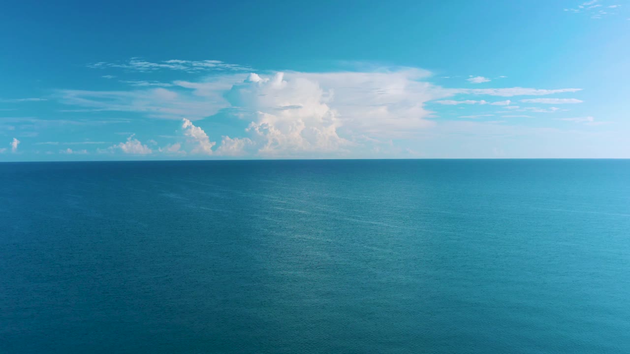 Wide aerial frame from the La Ribera coastline area with deep blue water below, pale cloud forms across the horizon, and no visible people or vessels.